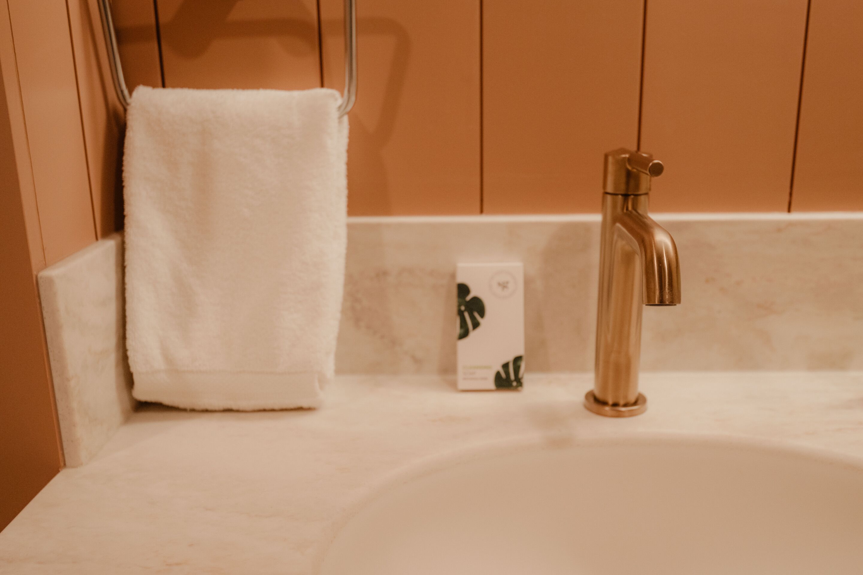 A bathroom with a white sink, a gold faucet, and a white towel hanging on a towel rack.