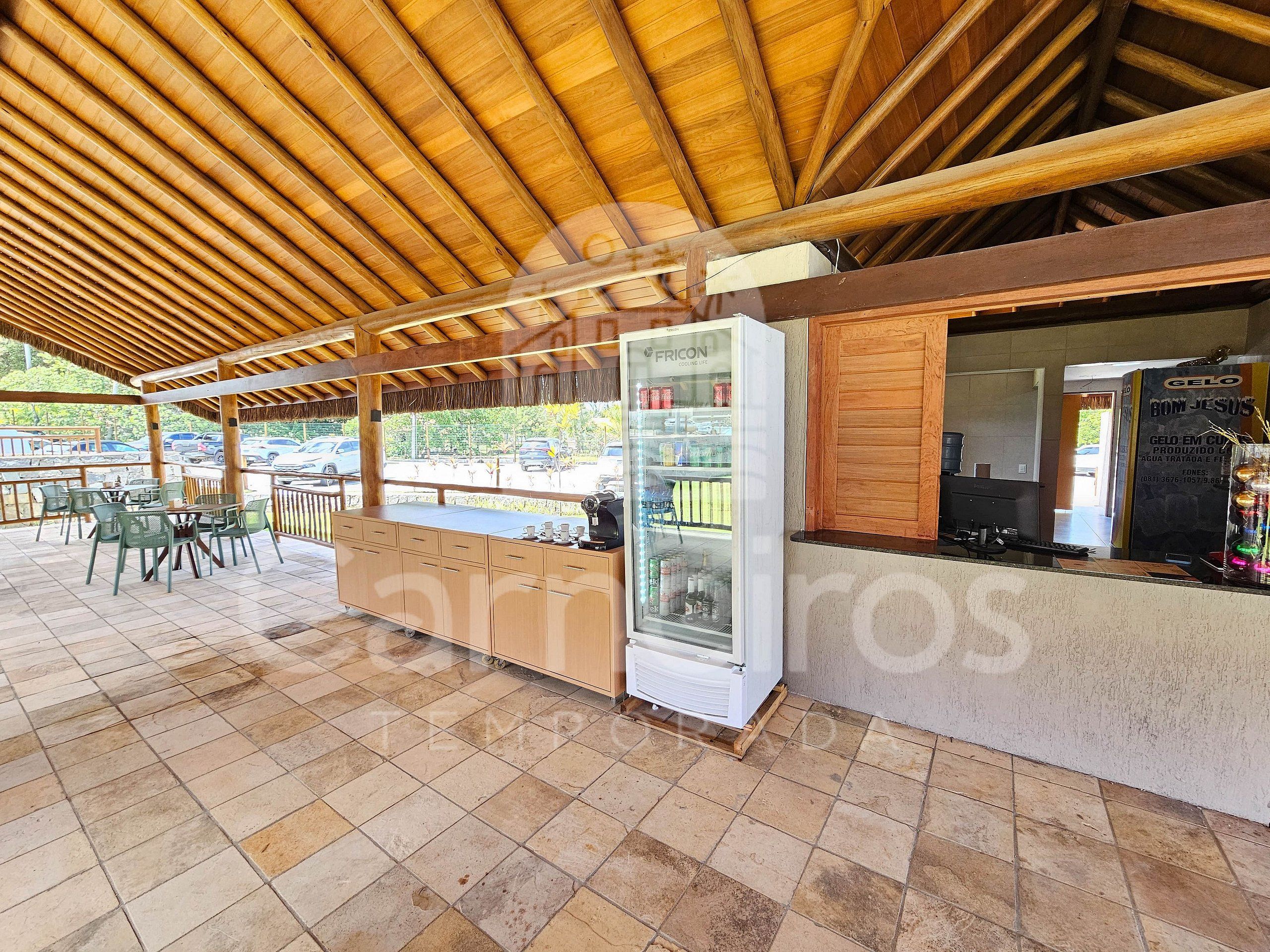 Un espacio de estar al aire libre techado, con techo de madera, un refrigerador de vidrio y una barra con un tablero de menú.