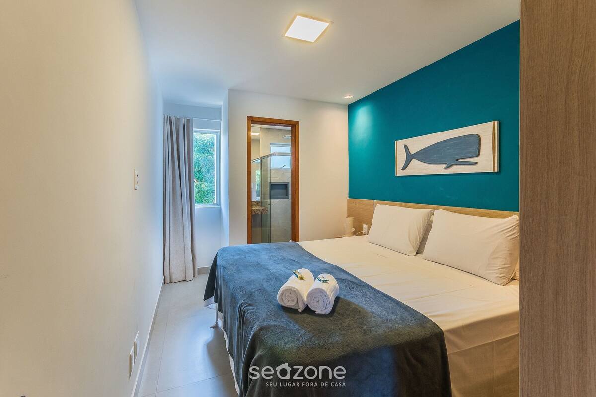 A hotel room with a bed, a teal accent wall, and a whale artwork.