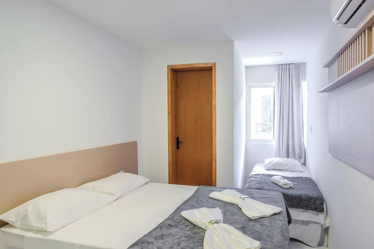 A hotel room with two beds, a wooden door, a window with curtains, and an air conditioning unit.