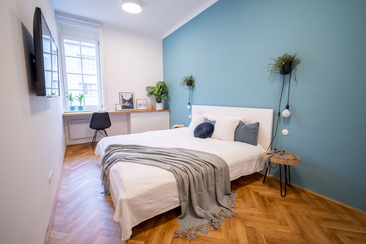 Un dormitorio con una cama, un escritorio y una silla. Hay dos macetas en la pared.