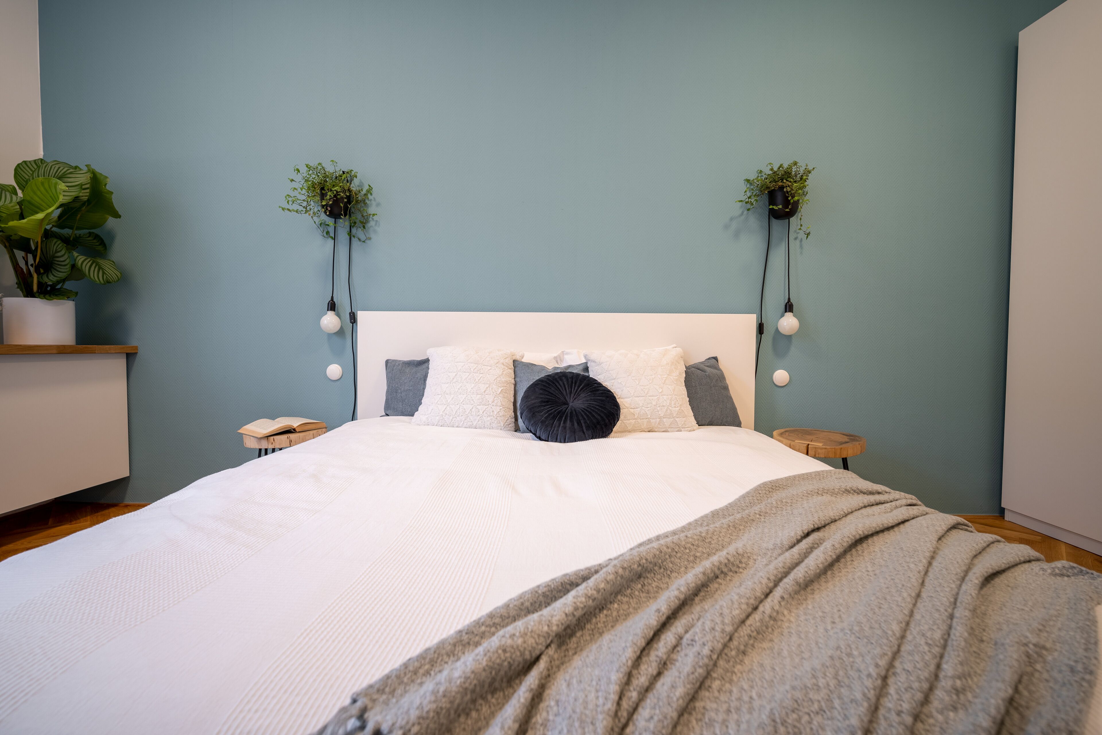 Una cama bien tendida con un cabecero blanco, dos mesitas de noche y dos lámparas de pared.