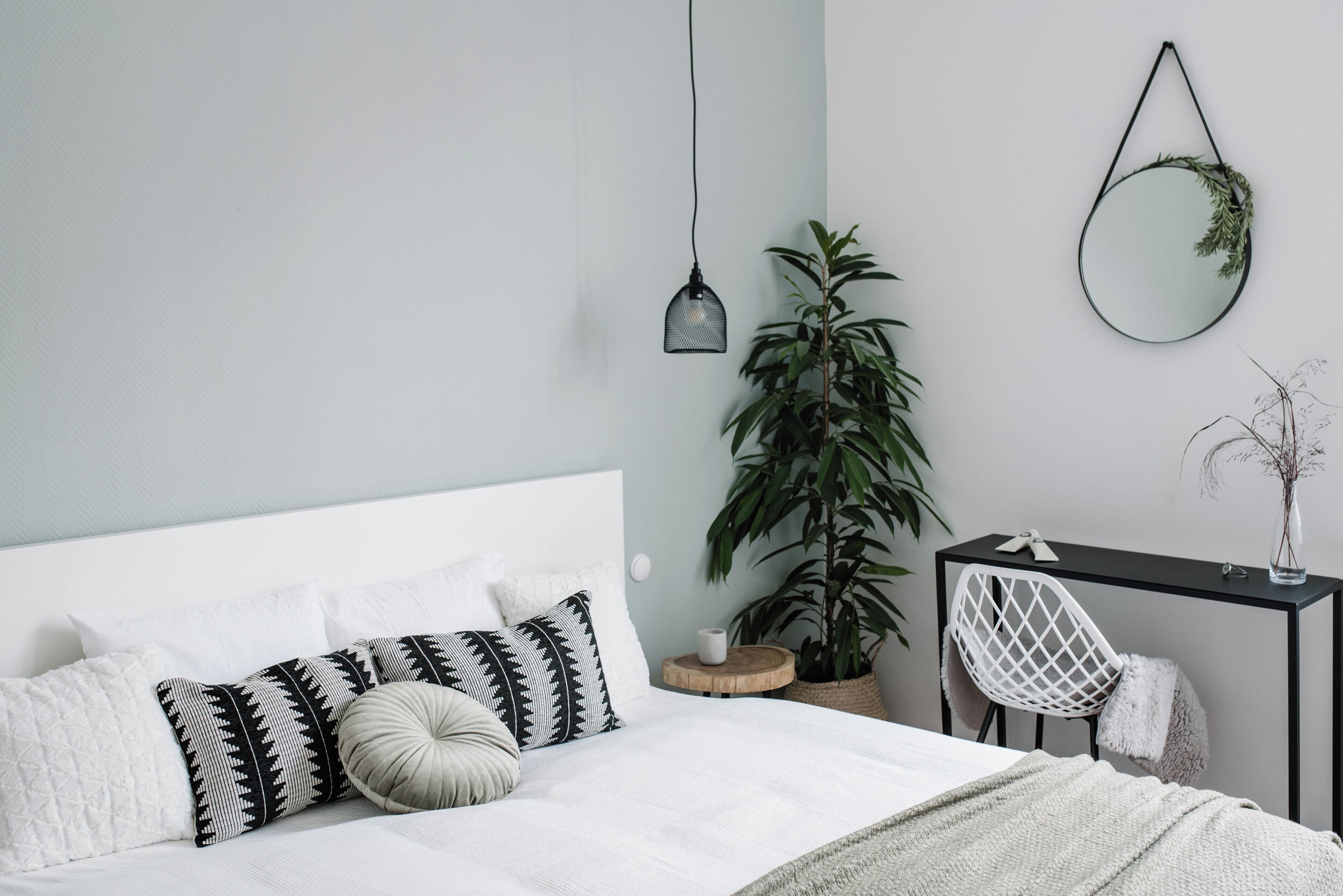 Une chambre à coucher bien rangée, avec un lit, une table de chevet, une chaise et un miroir suspendu.