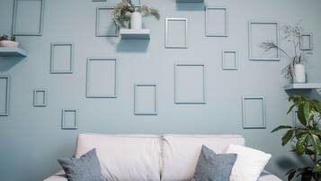 A room with a light blue wall, a white sofa with two pillows, and several white floating shelves with plants.