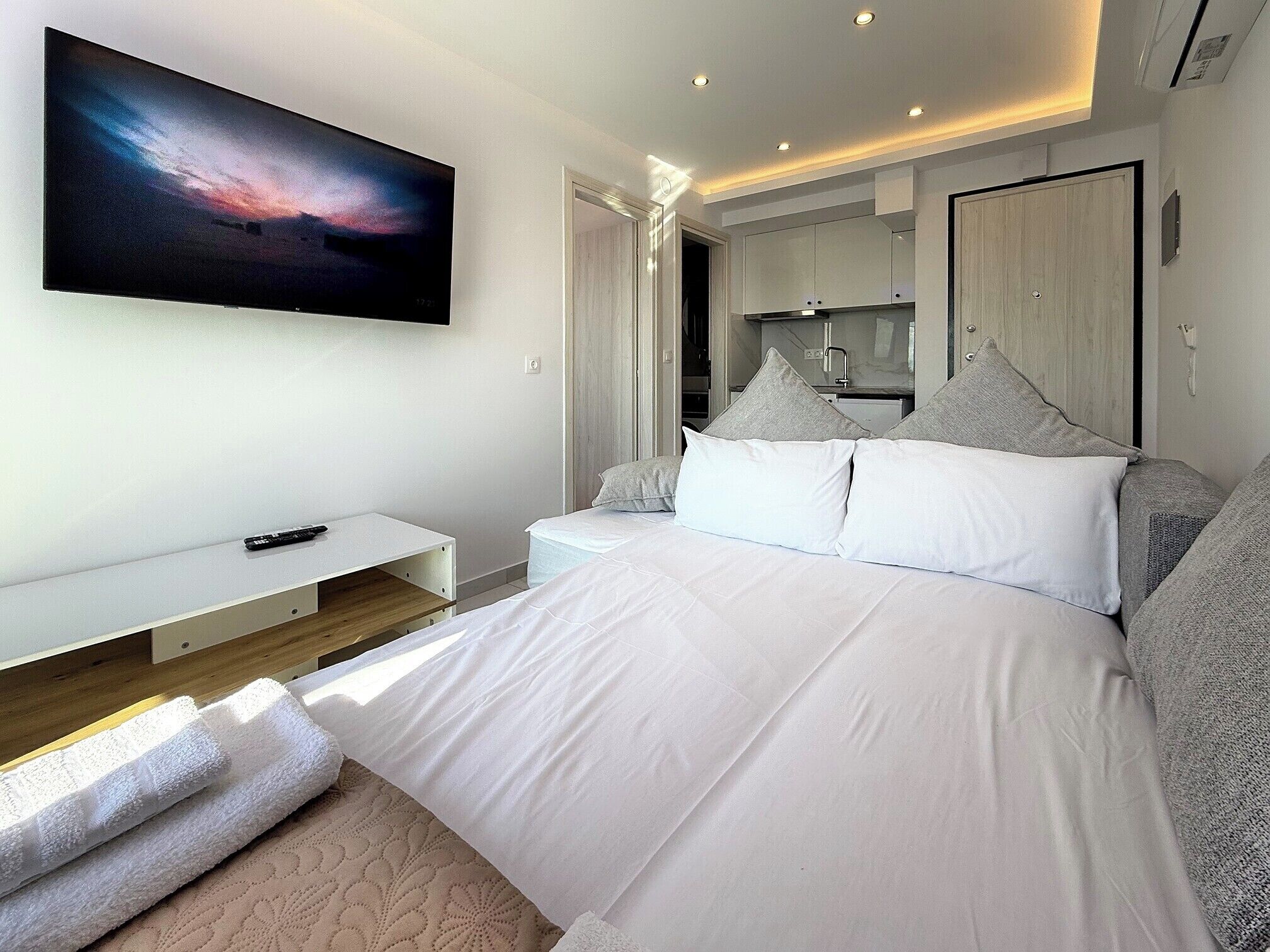 Un dormitorio moderno con una cama grande, un televisor montado en la pared y un escritorio pequeño.