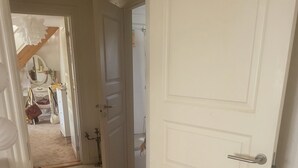En gang med en hvid dør, trægulv og en lille potteplante.