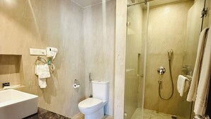 Un baño con suelo de mármol, lavabo blanco, inodoro y zona de ducha con cabina de vidrio.