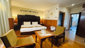 Habitación de hotel con una cama grande, dos mesitas de noche, suelo de madera y una zona de estar con dos sillones.
