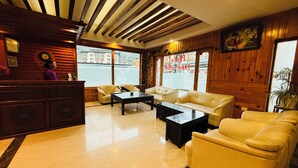 Un vestíbulo de hotel con techo de madera, una recepción, un conjunto de sofás y un ventanal con vista a la calle.