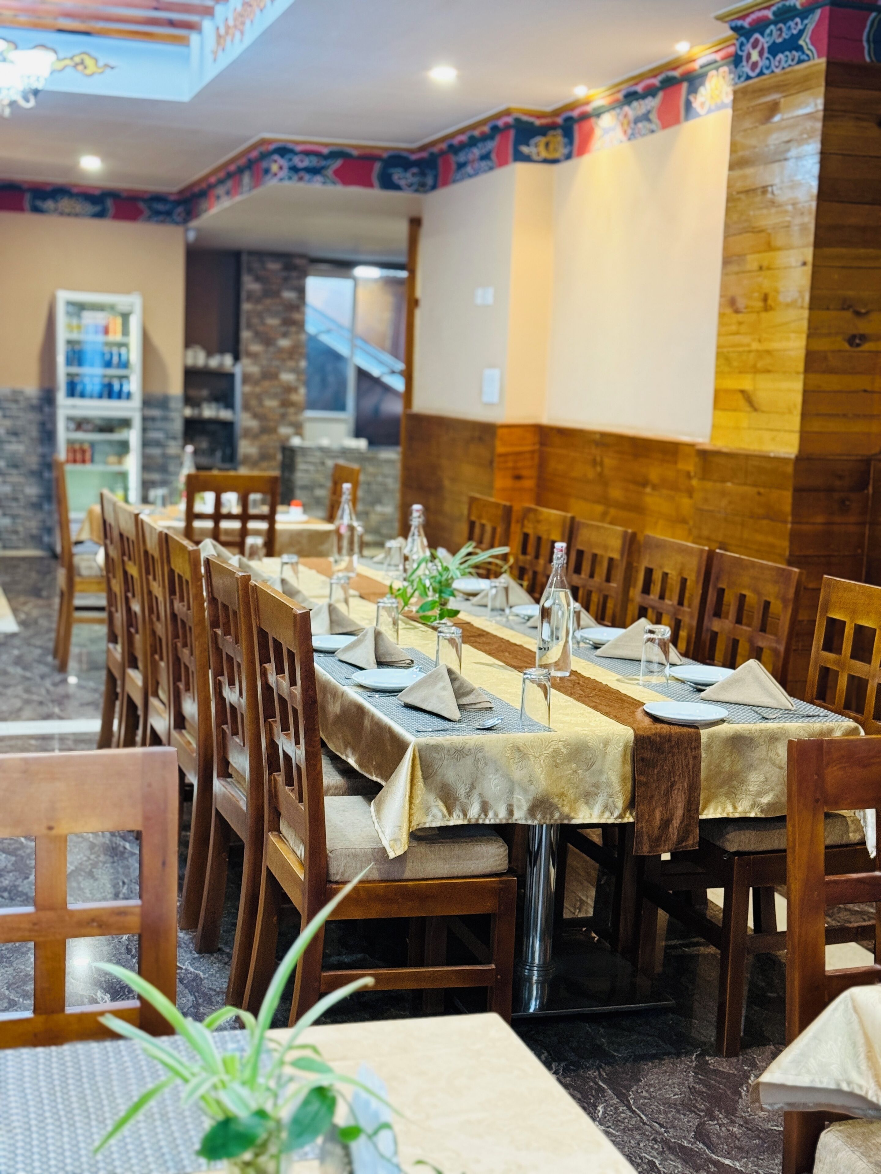 Een restaurant met een lange tafel gedekt voor een maaltijd, houten stoelen en een decoratief plafond.