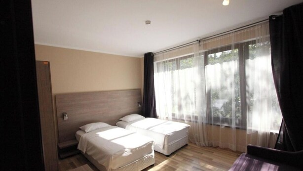 Une chambre d’hôtel avec deux lits, une grande fenêtre avec des rideaux légers et un plancher en bois.