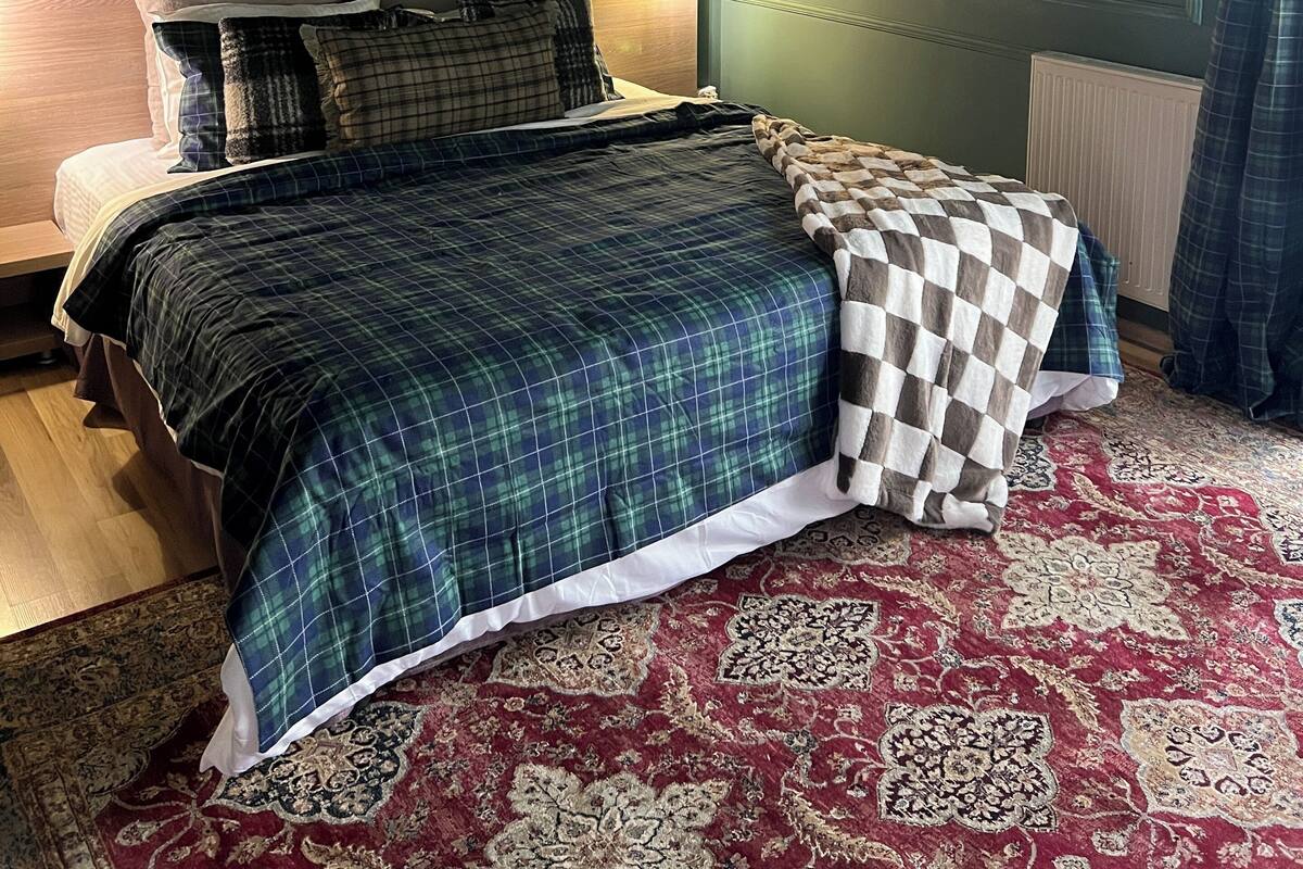 Ein Schlafzimmer mit Bett, einer Kopfteil, einer Wandleuchte, einer kleinen Segelboot-Dekoration und einem gemusterten Teppich.
