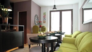 Un salon moderne avec un canapé vert, une table à manger avec des chaises et un coin cuisine comprenant un meuble et une plante.