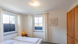 Een slaapkamer met twee bedden, een nachtkastje met een lamp, een houten garderobe en een decoratief wandobject.