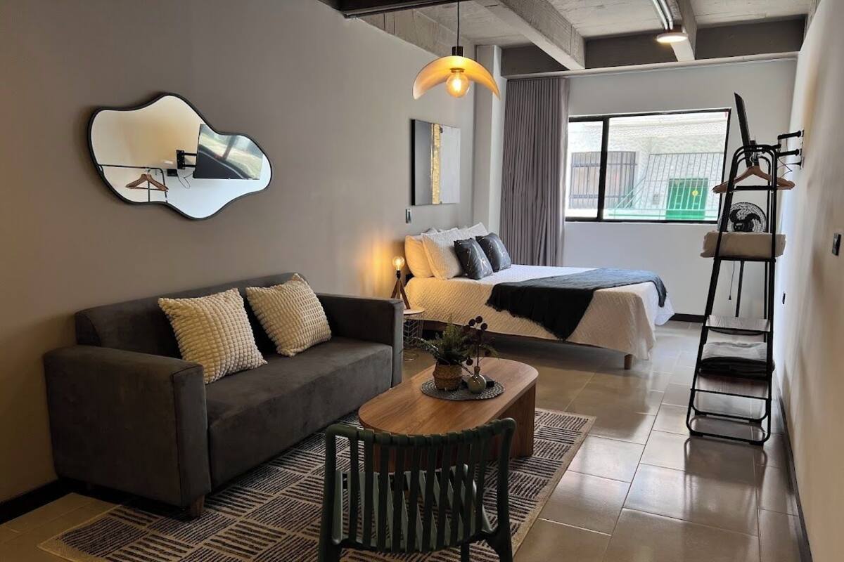 A modern room with a sofa, a bed, a coffee table, a hanging light fixture, and a mirror on the wall.