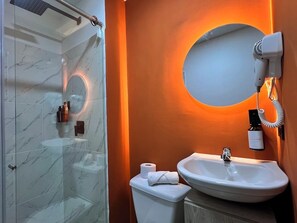 A bathroom with a glass shower, a white sink, and a hairdryer mounted on the wall. - Hotel Moore 45 (Medellín)