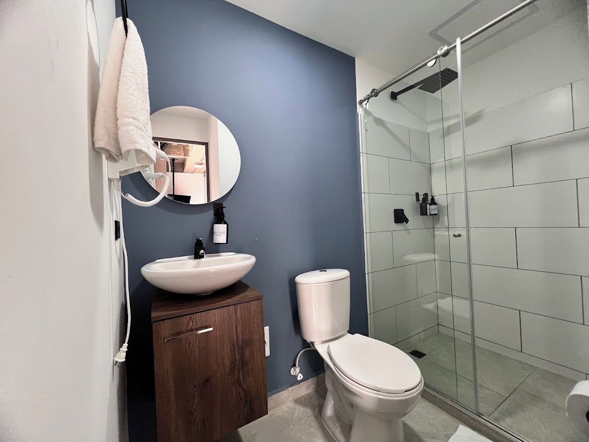 Een badkamer met een wit wastafelmeubel, een toilet, een glazen douchecabine en een spiegel.