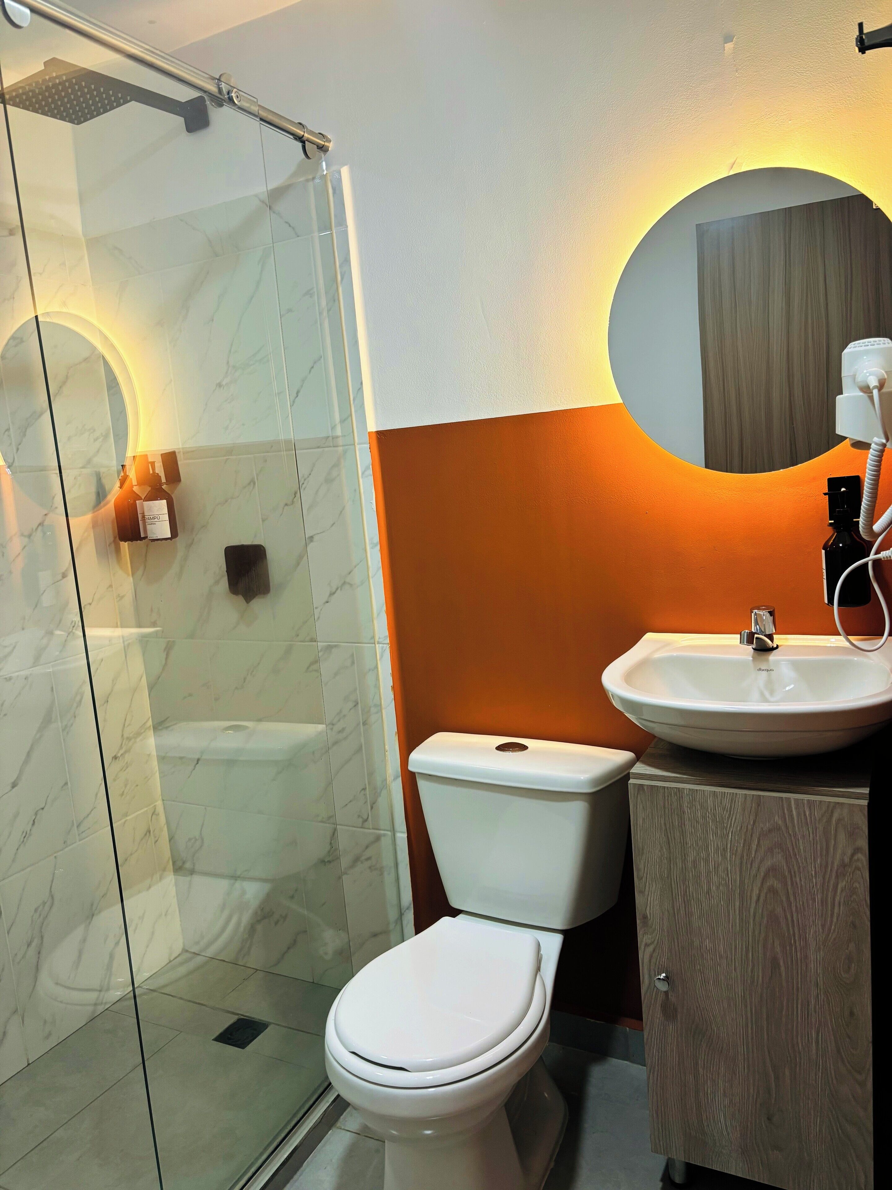 Een badkamer met een douche met glazen wand, een wit toilet en een wastafel met een houten kastje.