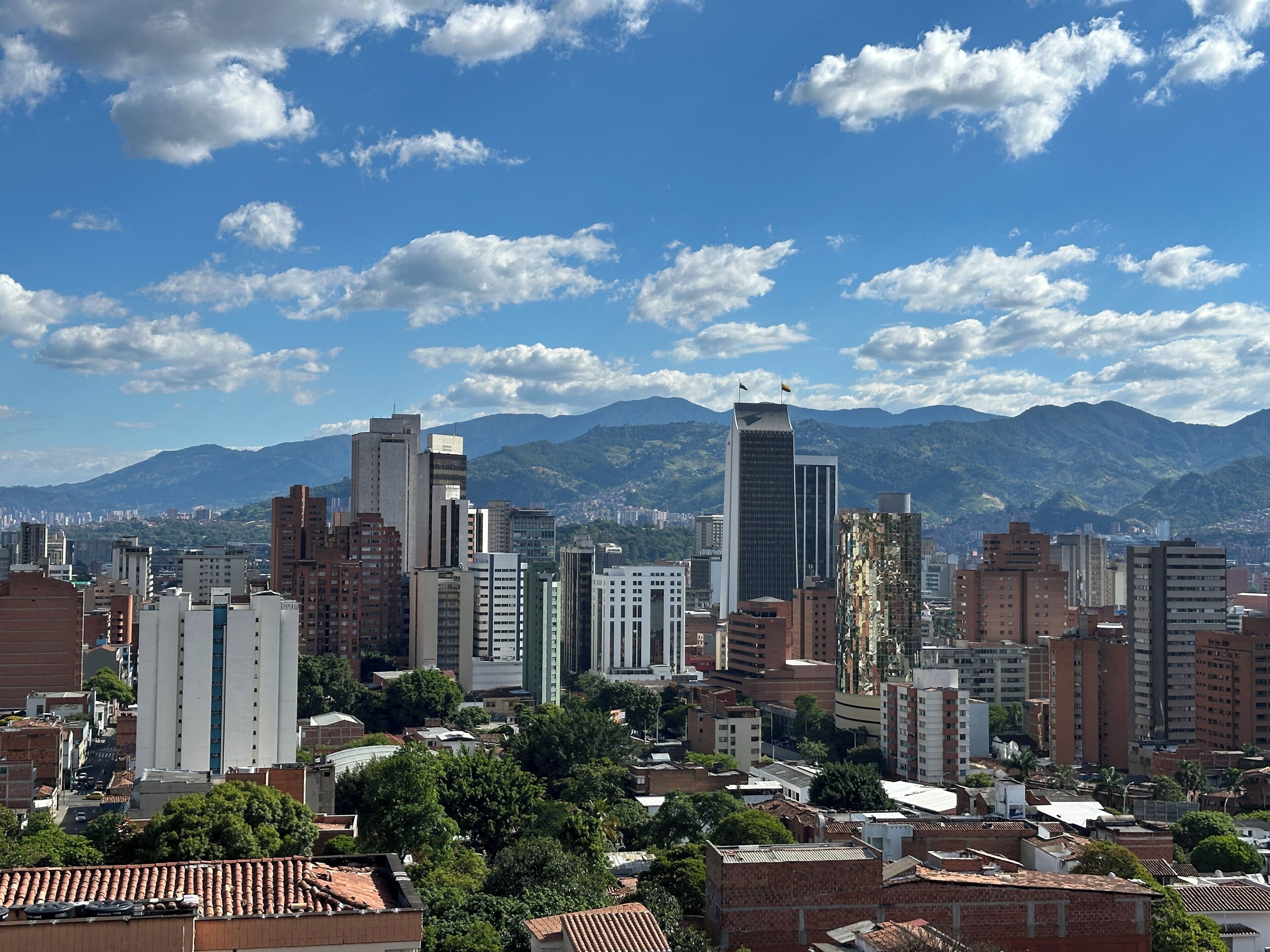 A cityscape with a variety of building heights, including modern high-rises and older structures, under a partly cloudy sky.