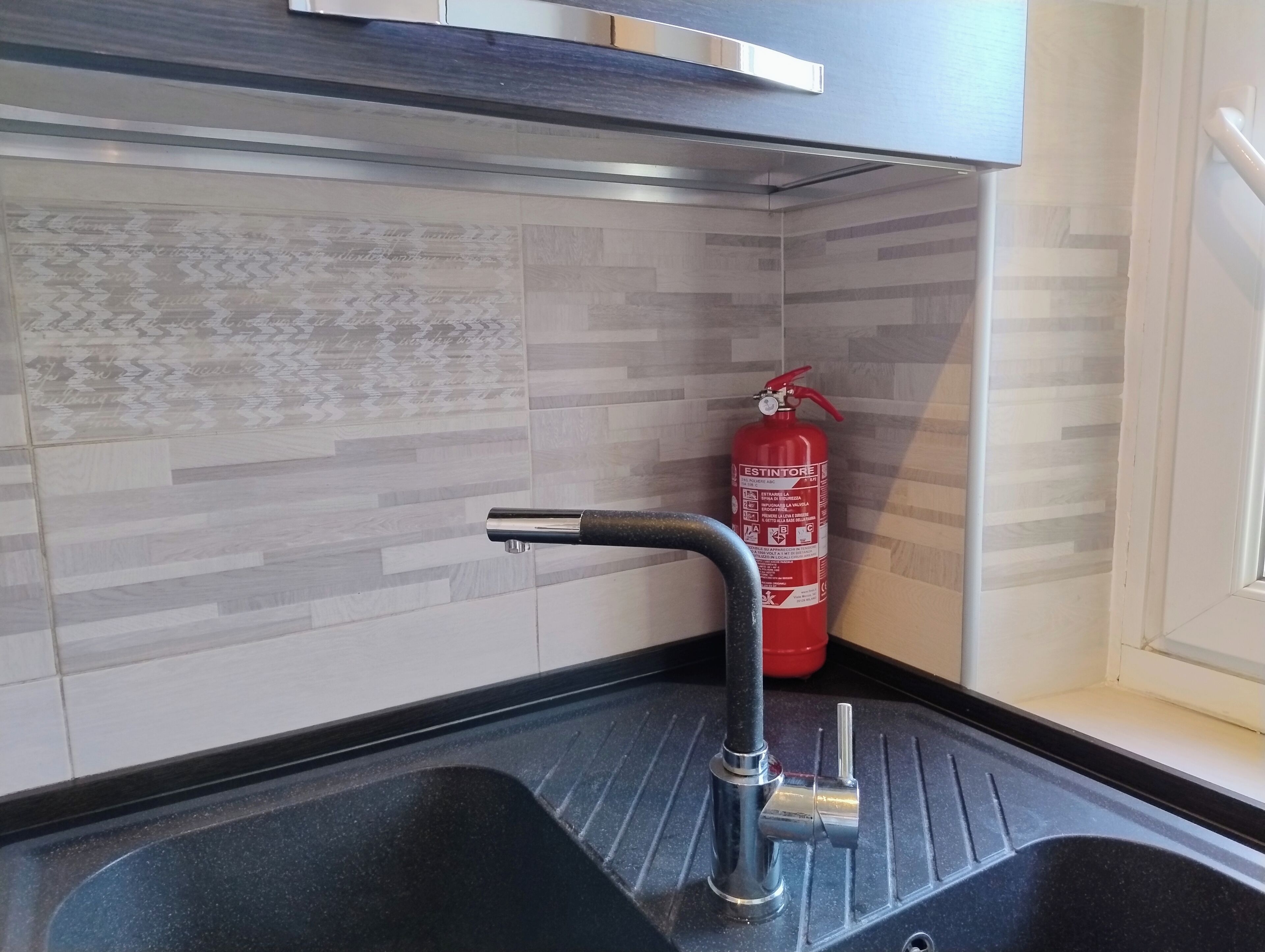 Et køkken med en moderne hane, en brandslukker og et mønstret backsplash.