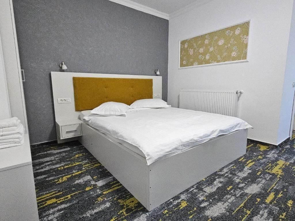 A hotel room with a bed, a nightstand, a radiator, and a wall with a floral pattern.