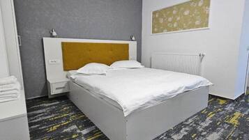 A hotel room with a bed, a nightstand, a radiator, and a wall with a floral pattern.