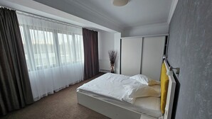 A hotel room with a large bed, a bedside table, a window with sheer curtains, and a radiator. - Hotel Ilinca (Jupiter)