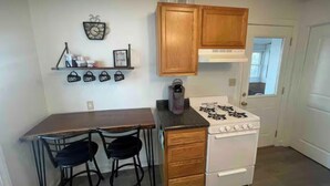 A small kitchen with wooden cabinets, a gas stove, a coffee maker, and two chairs. - Cozy Bungalow Retreat (Des Moines)
