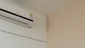 Una habitación de hotel con una cama, una colcha color beige y una toalla blanca doblada sobre la cama.