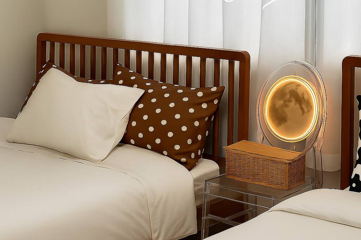 A hotel room with two beds, a wooden headboard, a bedside table with a lamp, and a mirror.