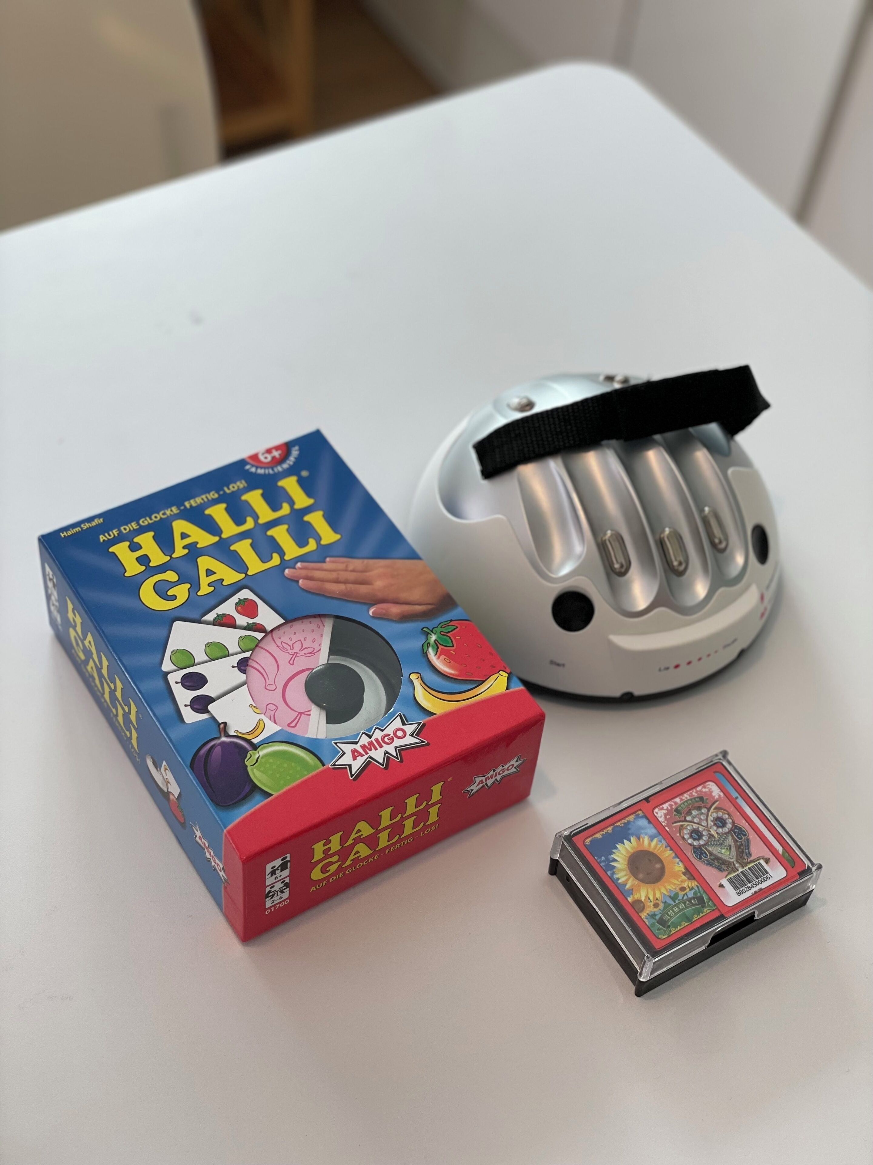 Ein weißer Tisch mit einem Gesellschaftsspiel, einem Helm und einem Kartenspiel.