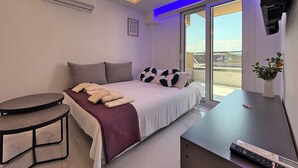 A modern bedroom with a bed, bedside table, and a view of the outdoors. - Deluxe One-Bedroom Suite No. 4 (Ground Floor) (Paralia)