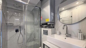 A modern bathroom with a glass-enclosed shower, a white sink with a mirror, and a toilet. - Deluxe One-Bedroom Suite No. 4 (Ground Floor) (Paralia)