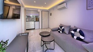 A modern living room with a grey sofa, two round tables, and a flat-screen TV mounted on the wall. - Deluxe One-Bedroom Suite No. 4 (Ground Floor) (Paralia)