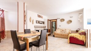 Ein Wohnzimmer mit einer Couch, einem Esstisch mit Stühlen, einer Küchenzeile und einem Flur, der in einen weiteren Raum führt.