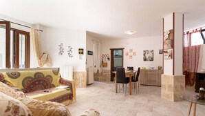 Ein Wohnzimmer mit Sofa, Esstisch, Stühlen und einer Küchenzeile mit Schränken und Arbeitsfläche.