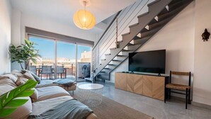 Een moderne woonkamer met een bank, een televisie, een trap en een groot raam.