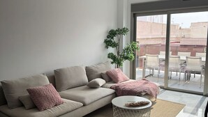 Een moderne woonkamer met een beige modulaire bank, een ronde salontafel en een groot raam met uitzicht op de stad.