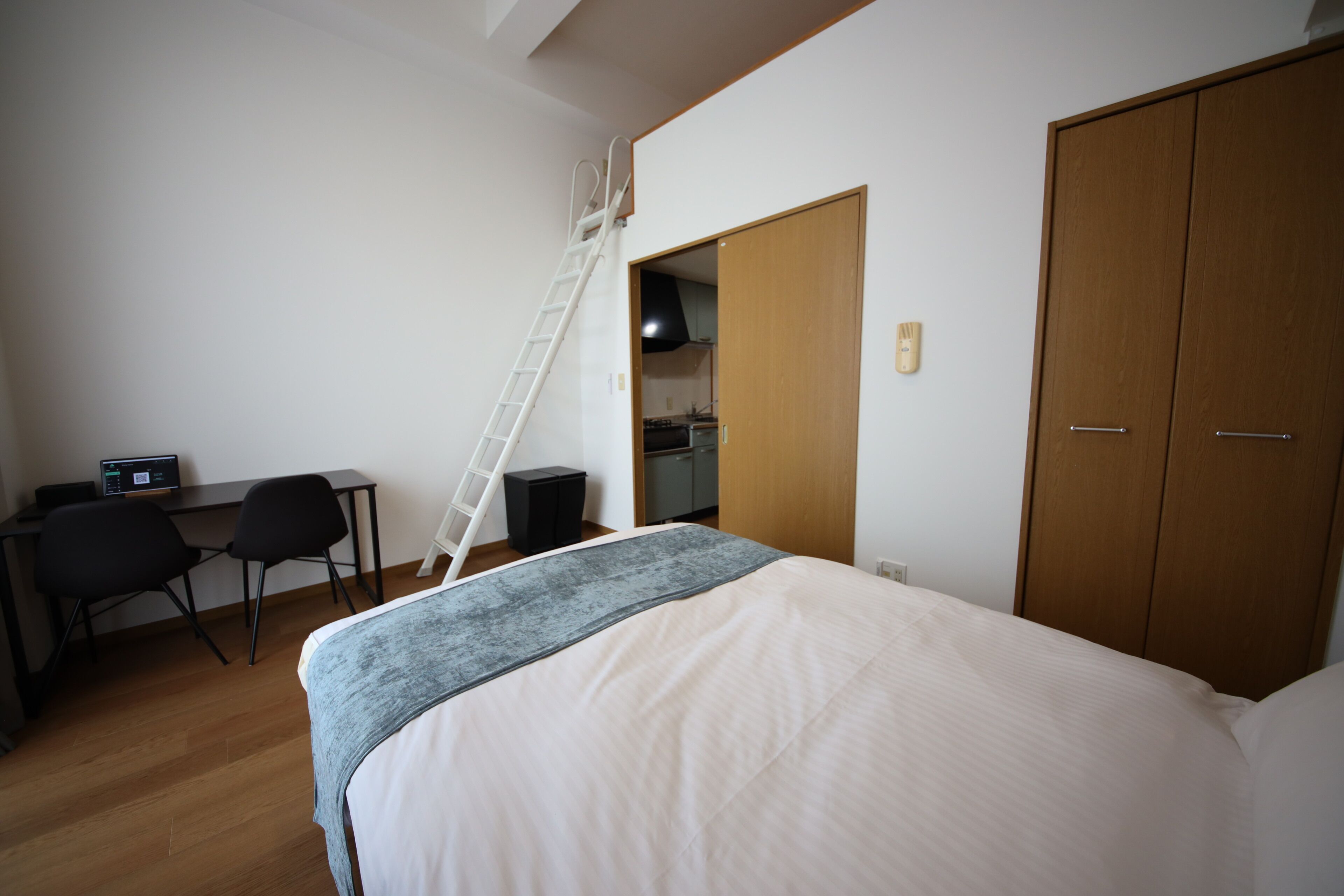 A bedroom with a bed, a desk with a computer, a chair, a wardrobe, and a ladder.
