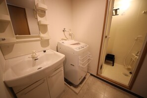 Un baño con lavamanos, lavadora y cabina de ducha con mampara de vidrio.