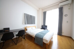 Un dormitorio con cama, escritorio, dos sillas, televisor y aire acondicionado.