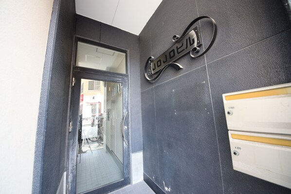 Fachada moderna de un edificio con puerta de vidrio, letrero de metal y panel informativo en la pared.