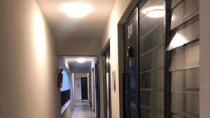 Un pasillo con puertas a la derecha, un extintor a la izquierda y suelo de baldosas.