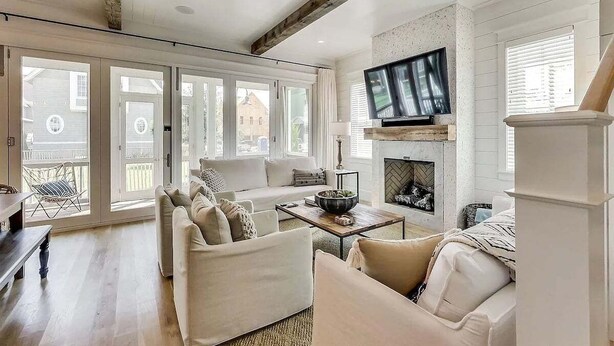 A spacious living room with a fireplace, a television mounted above it, and a large window overlooking a balcony. - Grace at Patience 12-Family Escape-Sleeps 10 (Inlet Beach)
