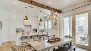 A spacious kitchen with white cabinets, a wooden island, and a dining area with wicker chairs. - Grace at Patience 12-Family Escape-Sleeps 10 (Inlet Beach)