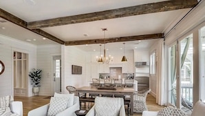 A spacious living room with a central dining area, large windows, and a modern chandelier. - Grace at Patience 12-Family Escape-Sleeps 10 (Inlet Beach)