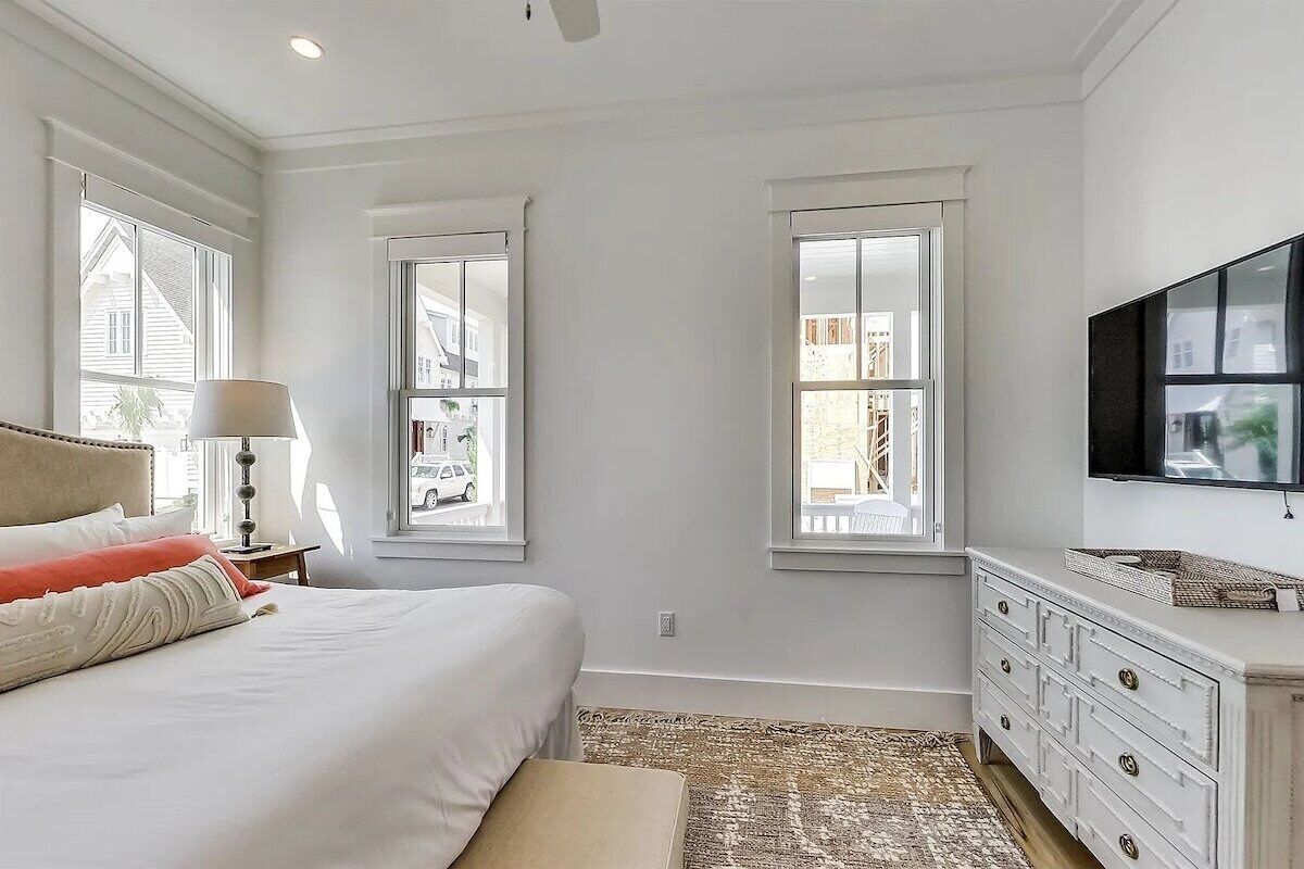 Une chambre à coucher avec un lit, une commode, une télévision et trois fenêtres.