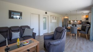 Ein modernes Wohnzimmer mit einer Couch, Sesseln, einem Couchtisch und einem Essbereich mit Stühlen und Tisch.