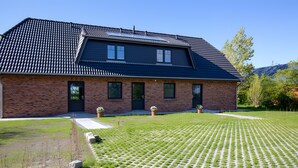 Ein zweistöckiges Backsteinhhaus mit dunklem Dach, einer gepflegten Rasenfläche mit einem Musterweg und einem kleinen Gartenbereich mit Blumentöpfen.