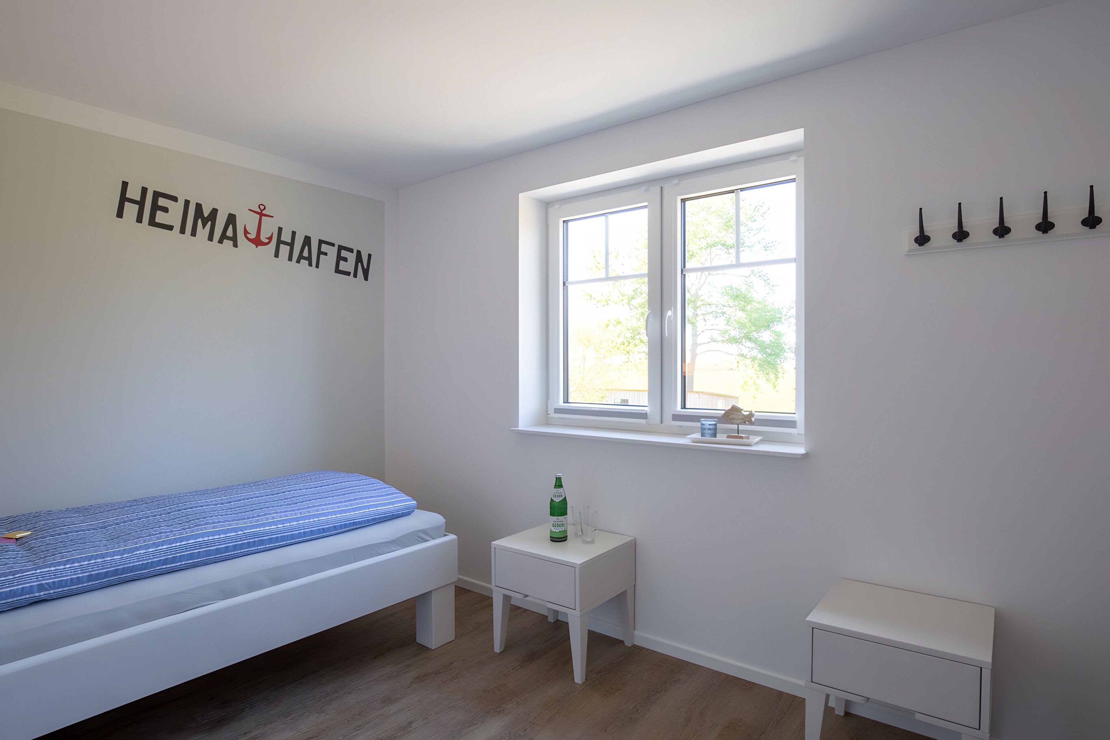 Un dormitorio con cama, una mesita de noche pequeña, una ventana y un perchero en la pared.